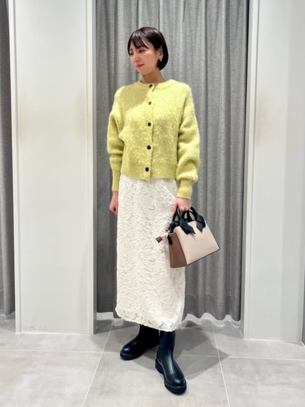 イエロー系のカーディガン/ボレロ、ホワイト系のスカートを着用したレディースの冬コーディネートの1枚目の写真