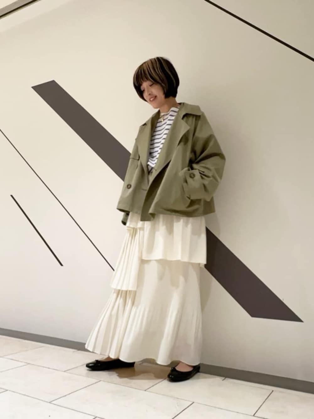 ホワイト系のスカート、ホワイト系のTシャツ/カットソー、グリーン系のトレンチコートを着用したレディースの冬コーディネートの1枚目の写真