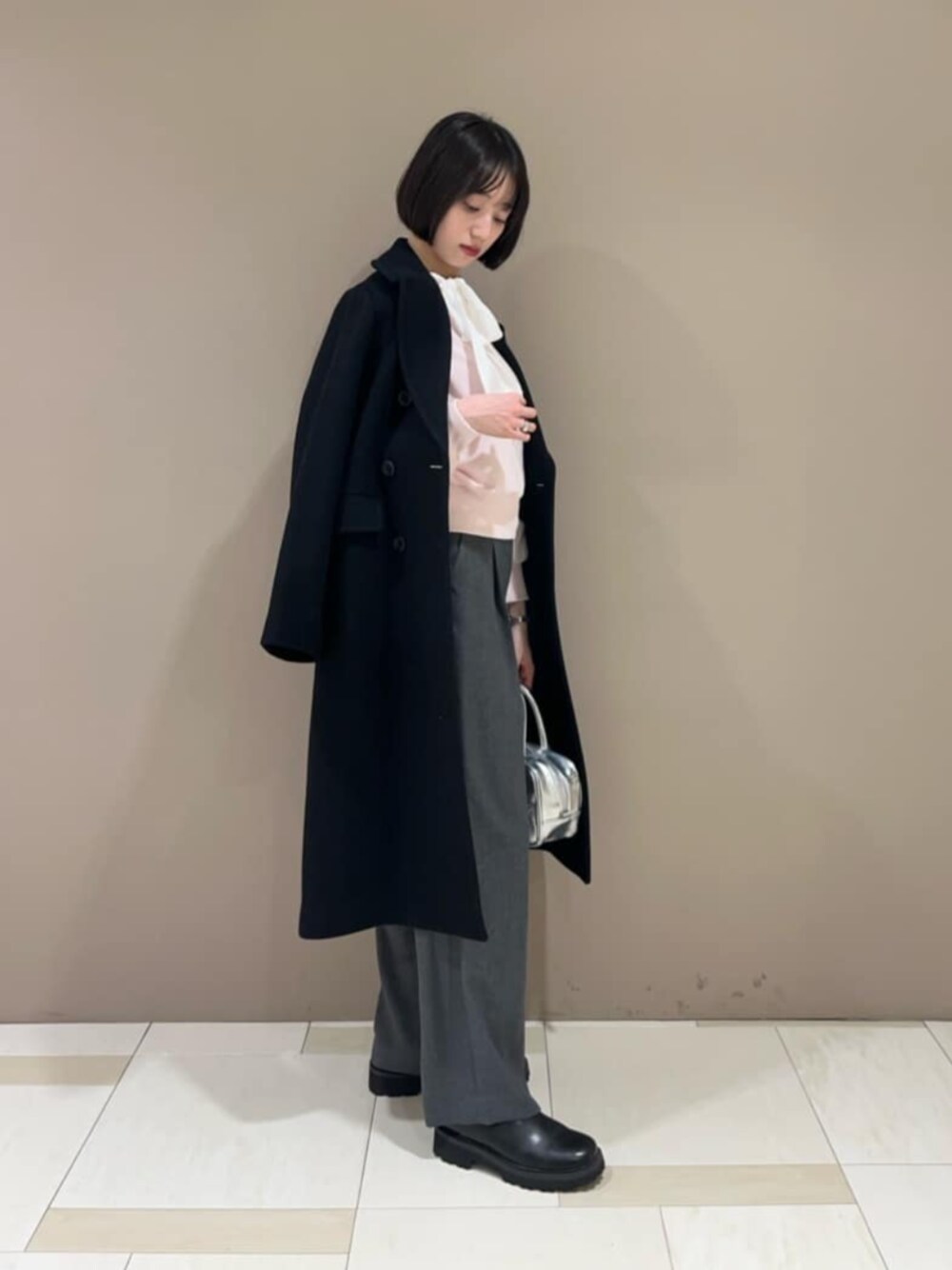 ブラック系のチェスターコート、ホワイト系のシャツ/ブラウス、グレー系のスラックスを着用したレディースの冬コーディネートの1枚目の写真