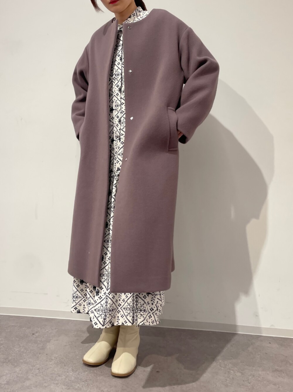 ブラウン系のノーカラーコート、ホワイト系のワンピースを着用したレディースの冬コーディネートの1枚目の写真