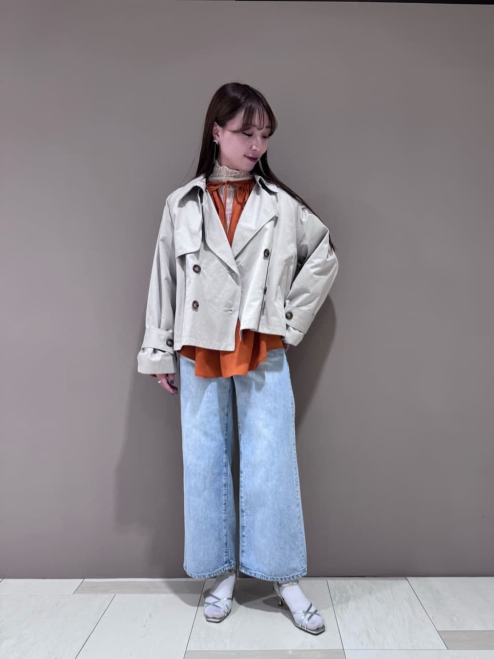 ホワイト系のトレンチコート、ブルー系のデニムパンツ、シルバー系のサンダルを着用したレディースの春コーディネートの1枚目の写真