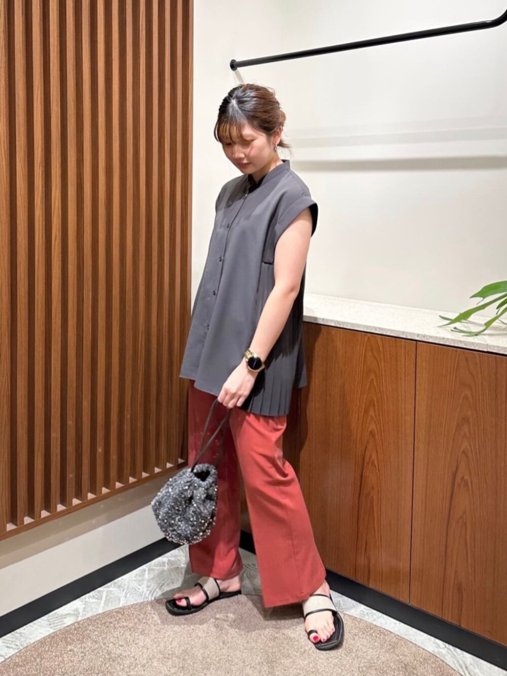 レッド系のスラックス、グレー系のシャツ/ブラウス、グレー系のビジネスバッグを着用したレディースの夏コーディネートの1枚目の写真