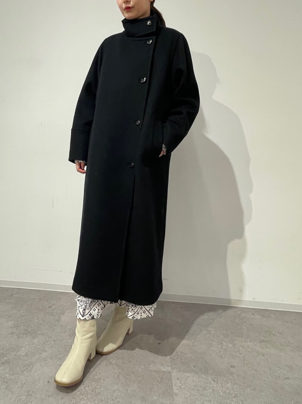 ブラック系のステンカラーコート、ホワイト系のワンピースを着用したレディースの冬コーディネートの1枚目の写真