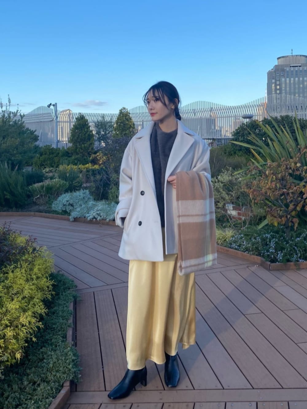 グレー系のニット/セーター、ホワイト系のピーコート、イエロー系のスカートを着用したレディースの冬コーディネートの1枚目の写真