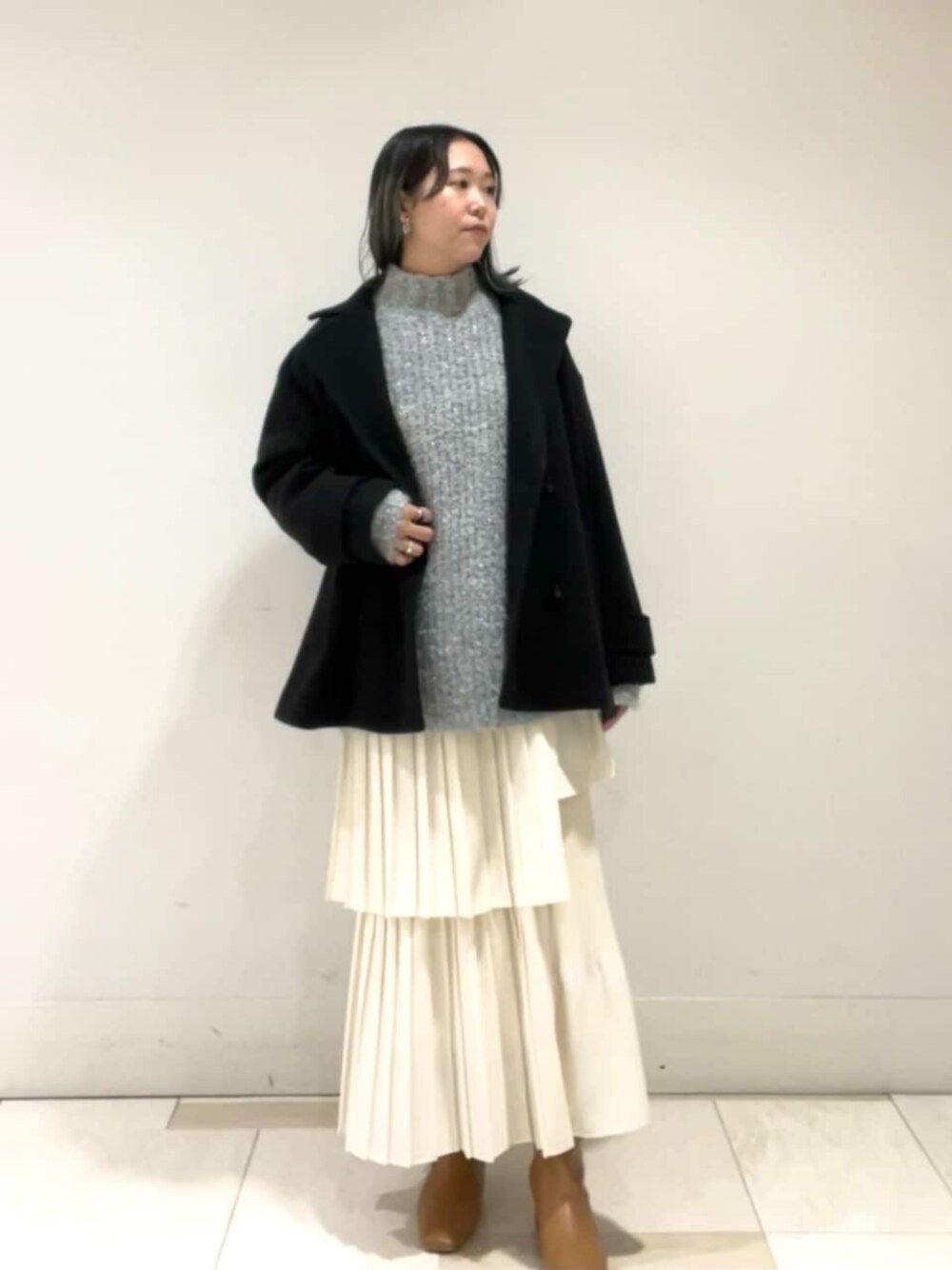 ベージュ系のブーツ、ホワイト系のスカート、ブラック系のピーコートを着用したレディースの冬コーディネートの1枚目の写真