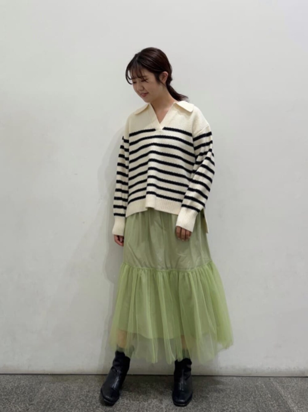 ブラック系のブーツ、ホワイト系のニット/セーター、グリーン系のスカートを着用したレディースの秋コーディネートの1枚目の写真