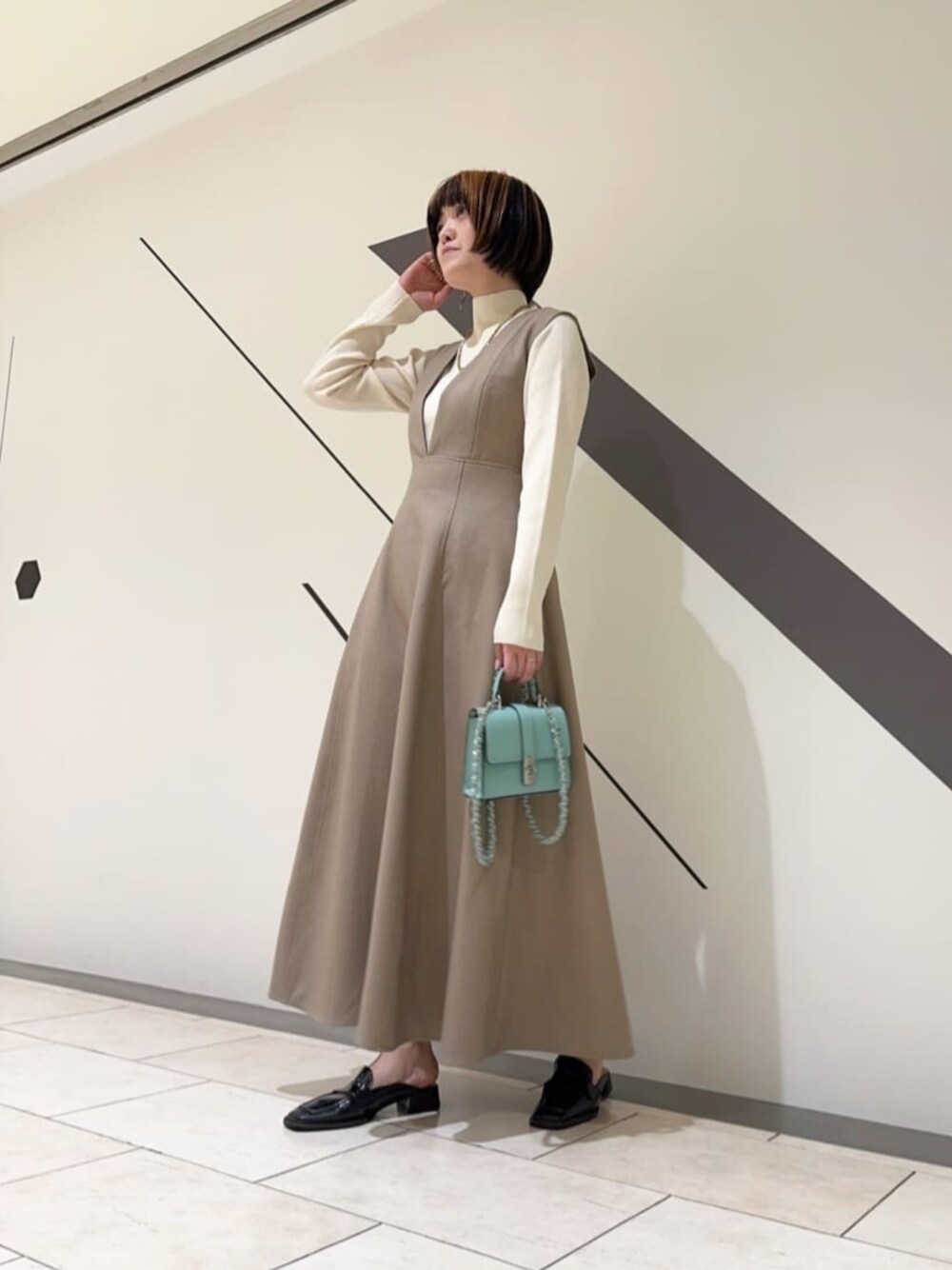 ブルー系のショルダーバッグ、ブラウン系のジャンパースカート、ホワイト系のニット/セーターを着用したレディースの春コーディネートの1枚目の写真