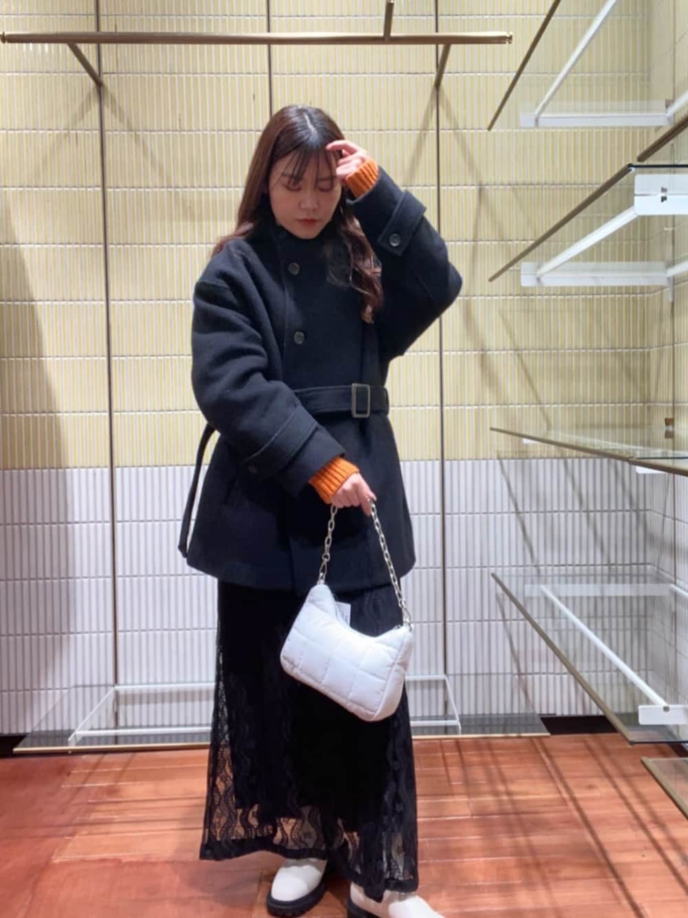 ホワイト系のビジネスバッグ、ホワイト系のブーツ、オレンジ系のニット/セーターを着用したレディースの冬コーディネートの1枚目の写真