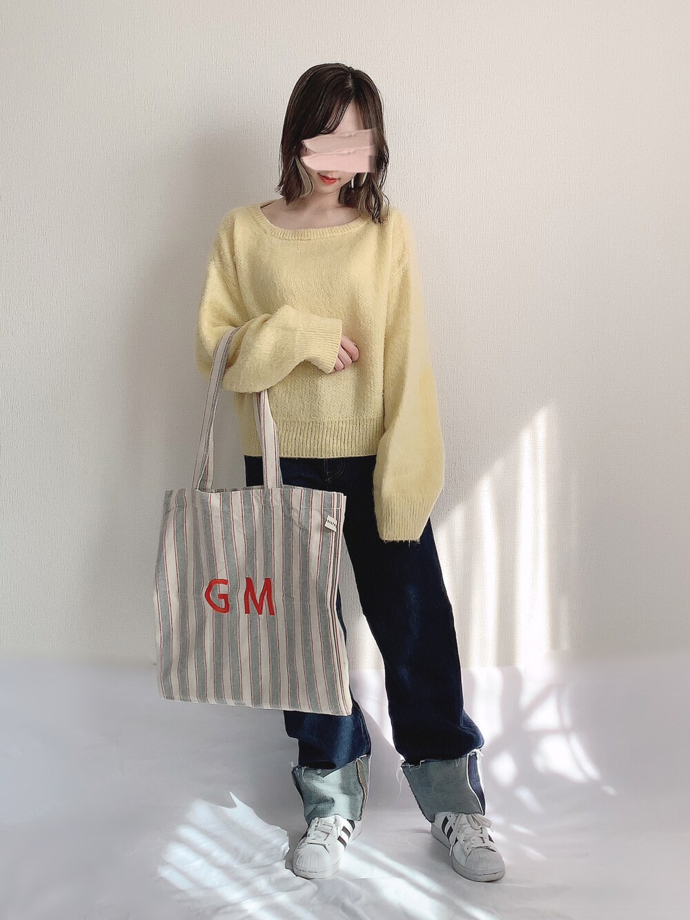 イエロー系のニット/セーター、ブルー系のデニムパンツ、グレー系のトートバッグを着用したレディースの秋コーディネートの1枚目の写真
