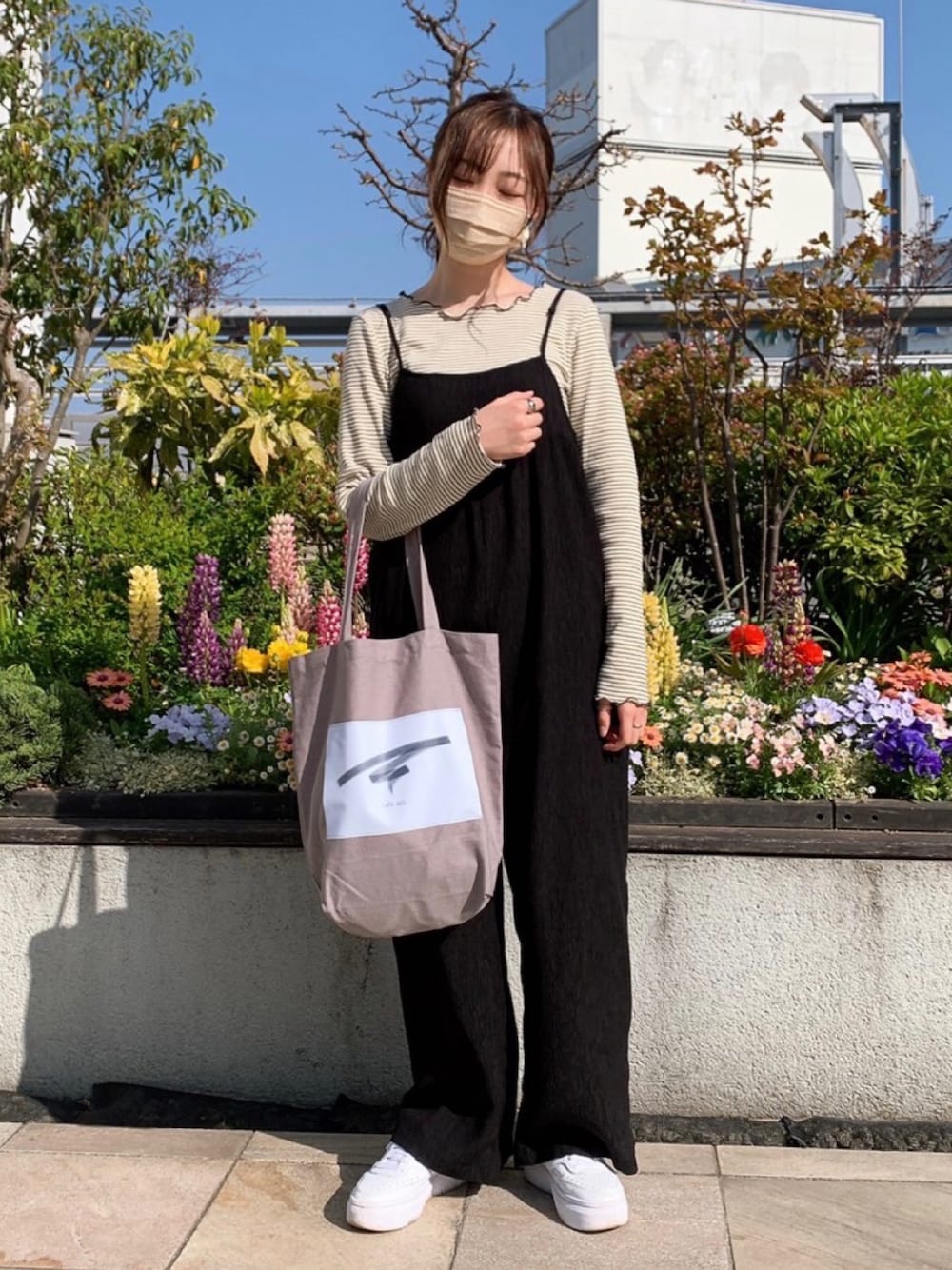 グレー系のトートバッグ、ベージュ系のトップス、ブラック系のサロペット/オーバーオールを着用したレディースの春コーディネートの1枚目の写真