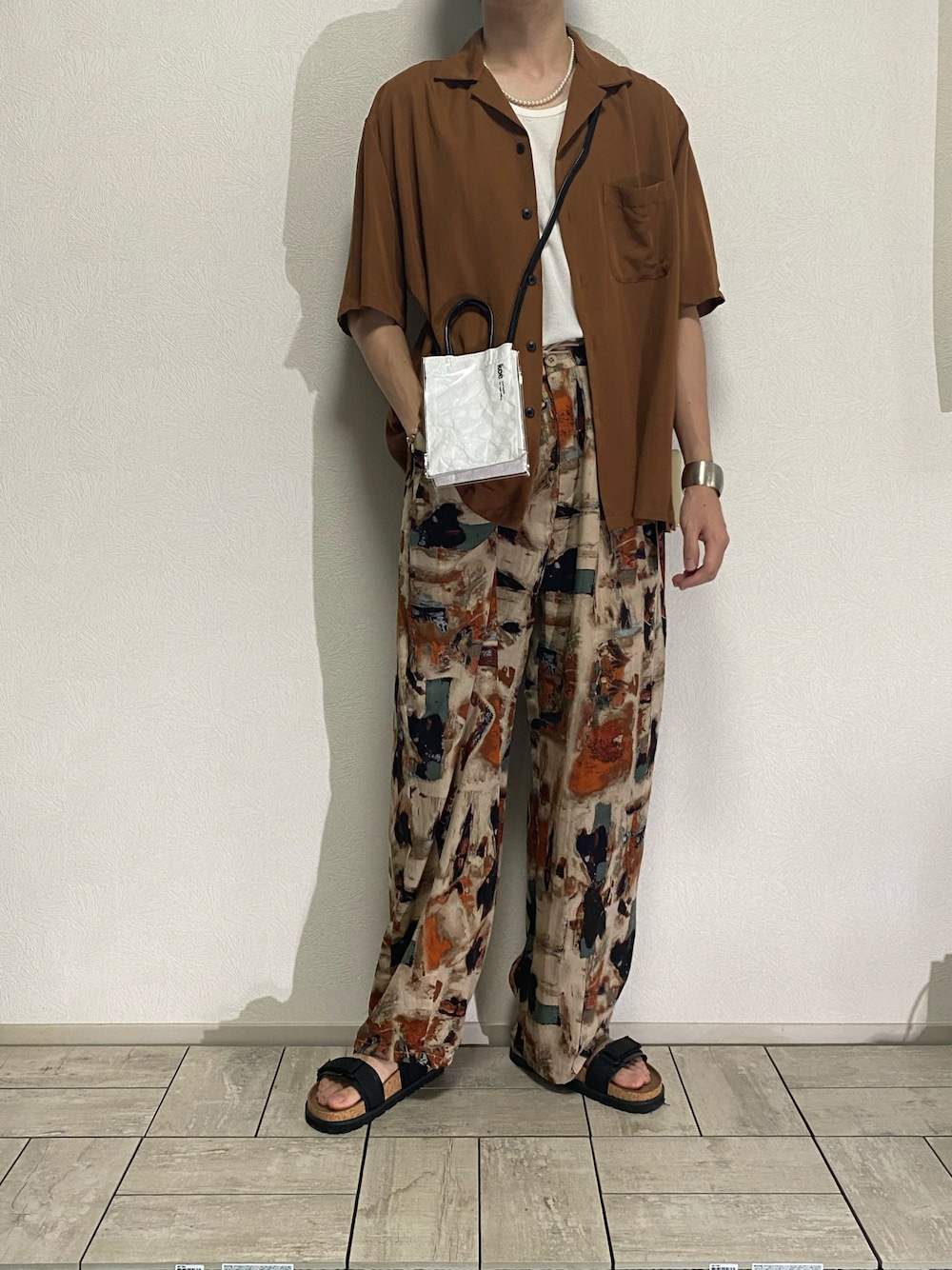 ホワイト系のトートバッグ、ブラウン系のその他パンツ、オレンジ系のポロシャツを着用したメンズの夏コーディネートの1枚目の写真
