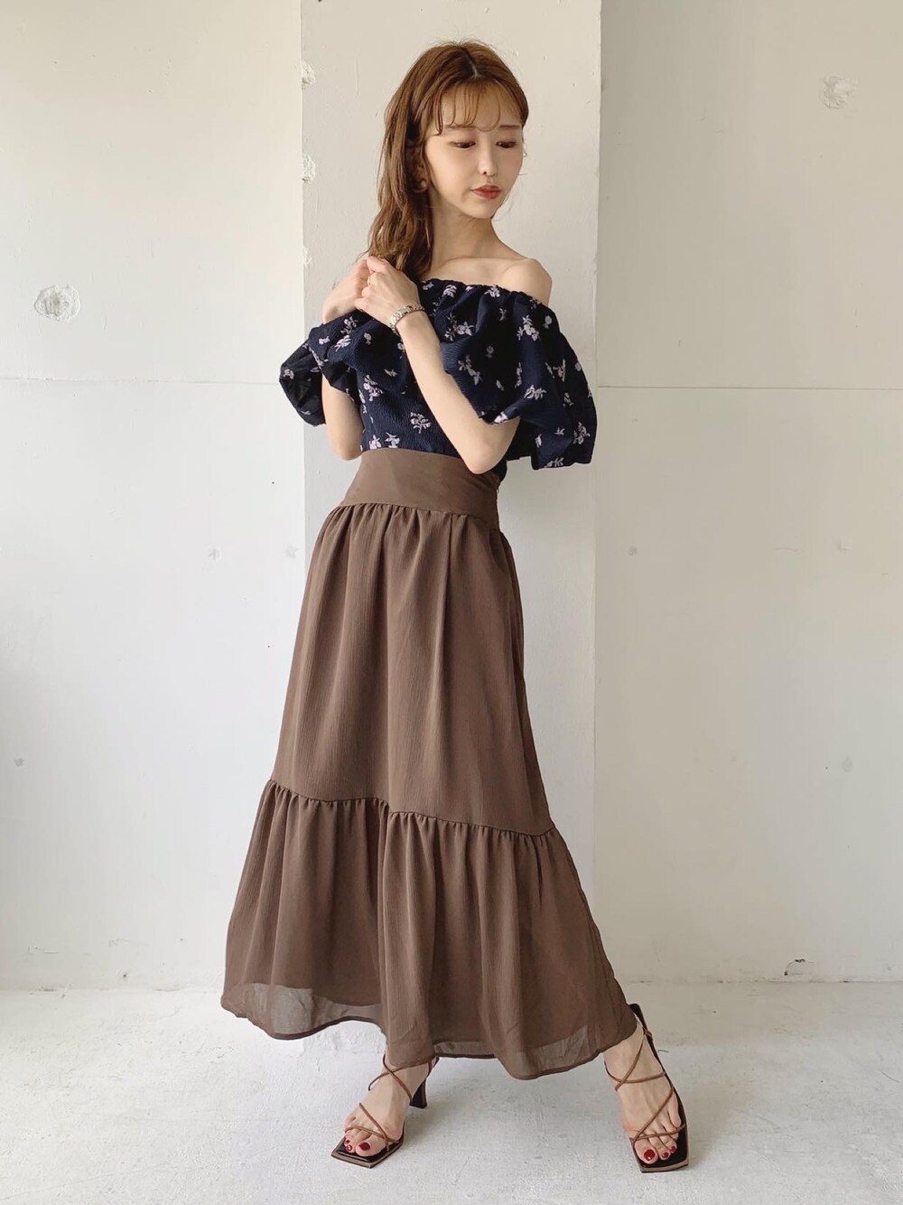 ブラウン系のスカート、ブラウン系のサンダル、ブルー系のシャツ/ブラウスを着用したレディースの夏コーディネートの1枚目の写真