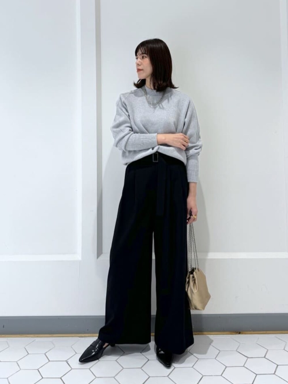 グレー系のニット/セーター、ブラック系のその他パンツ、ゴールド系のショルダーバッグを着用したレディースの冬コーディネートの1枚目の写真