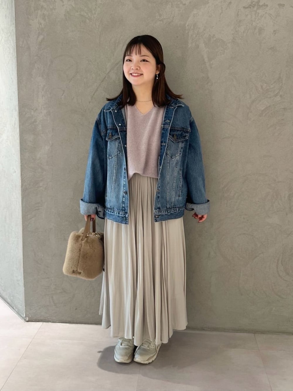 ベージュ系のスカート、ブルー系のデニムジャケット、ベージュ系のハンドバッグを着用したレディースの冬コーディネートの1枚目の写真