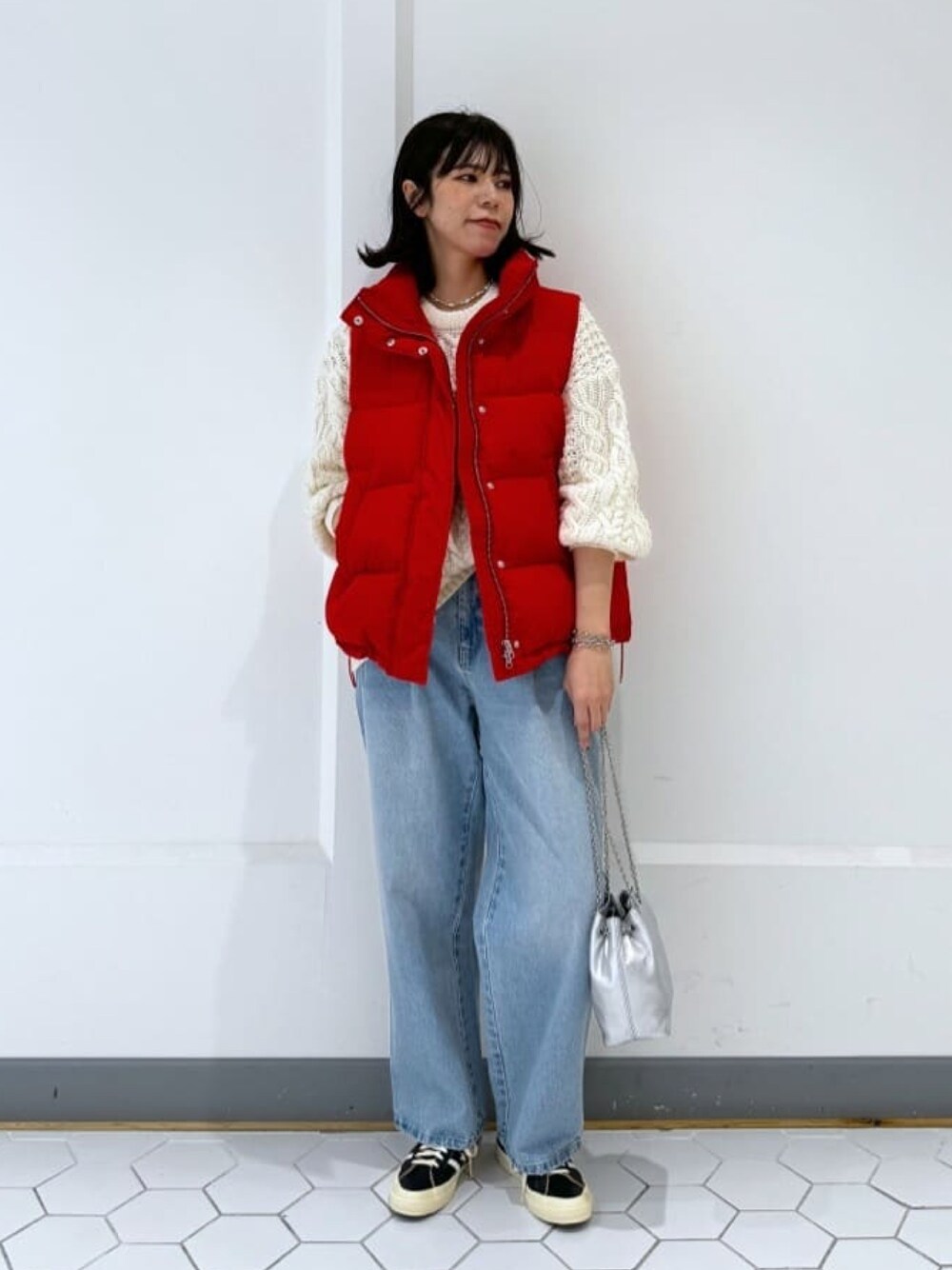 レッド系のダウンベスト、ブルー系のデニムパンツ、ホワイト系のニット/セーターを着用したレディースの冬コーディネートの1枚目の写真