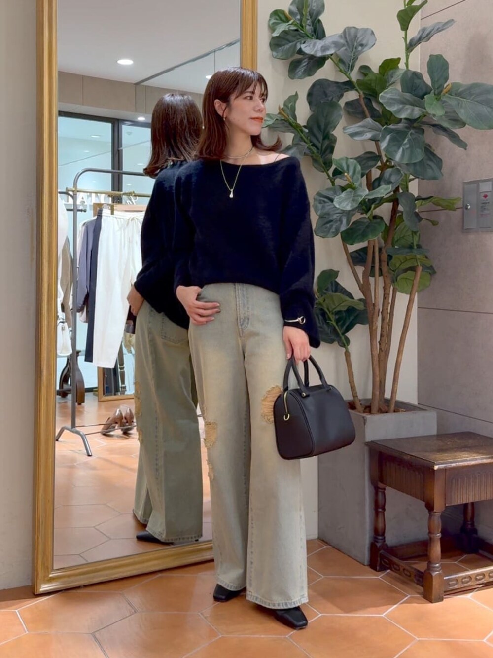 ブラック系のニット/セーター、ブラック系のボストンバッグ、ブルー系のデニムパンツを着用したレディースの秋コーディネートの1枚目の写真