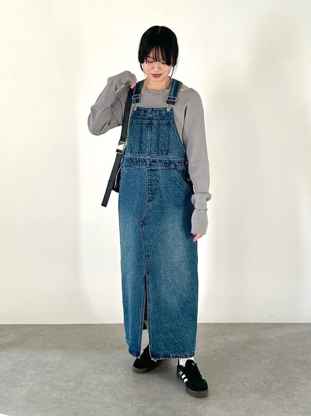 ブルー系のジャンパースカート、グレー系のニット/セーター、ブラック系のボディバッグ/ウエストポーチを着用したレディースの冬コーディネートの1枚目の写真