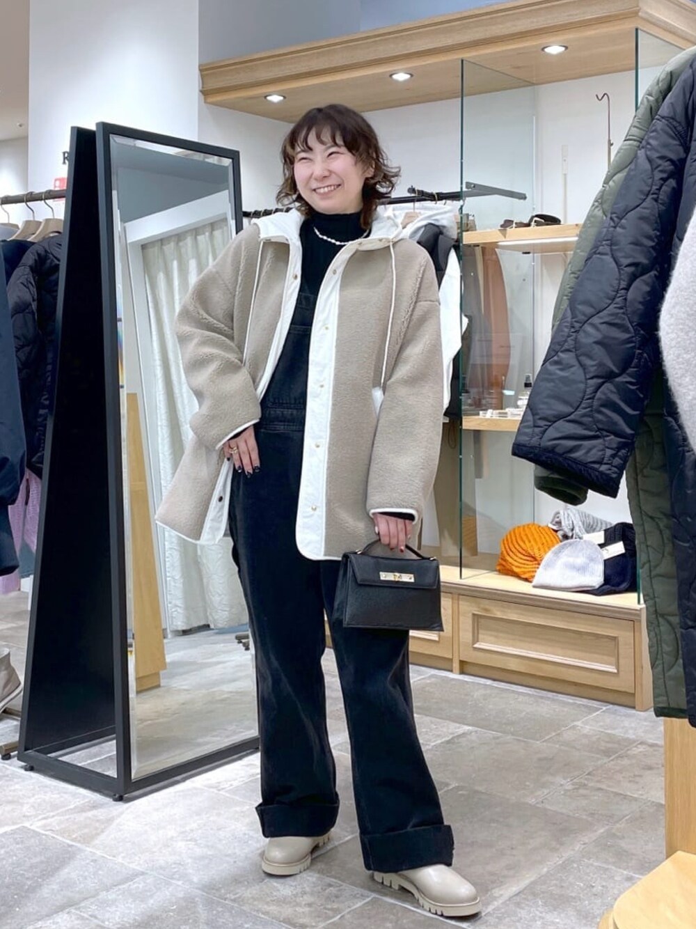 ベージュ系のその他アウター、ブラック系のサロペット/オーバーオール、ブラック系のハンドバッグを着用したレディースの冬コーディネートの1枚目の写真