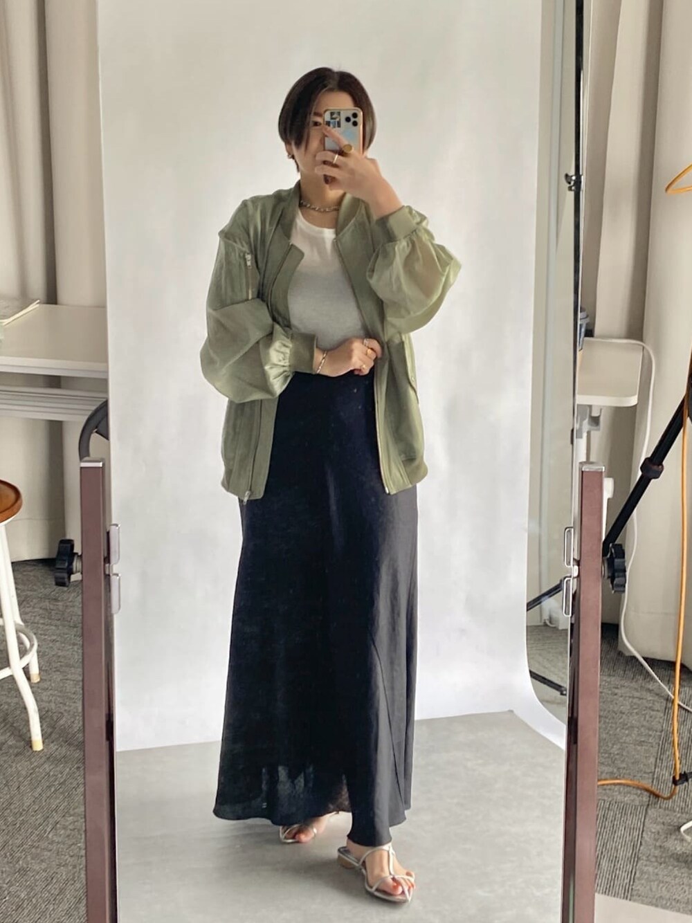 ブラック系のスカート、シルバー系のサンダル、ベージュ系のブルゾンを着用したレディースの春コーディネートの1枚目の写真