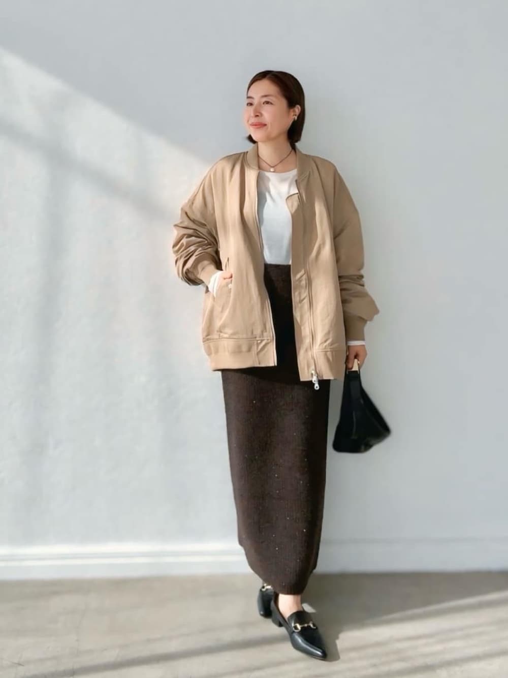 ブラウン系のスカート、ベージュ系のブルゾン、ホワイト系のTシャツ/カットソーを着用したレディースの秋コーディネートの1枚目の写真