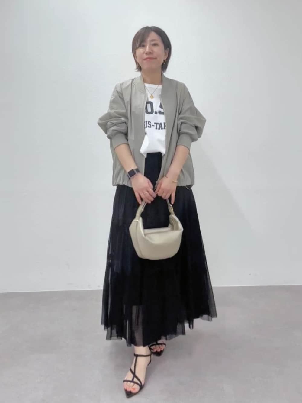 ブラック系のサンダル、ゴールド系のショルダーバッグ、グリーン系のブルゾンを着用したレディースの春コーディネートの1枚目の写真