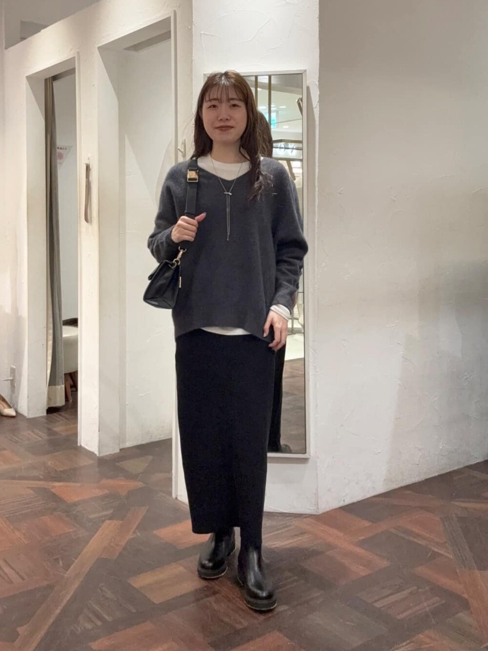 グレー系のニット/セーター、ホワイト系のTシャツ/カットソー、ブラック系のスカートを着用したレディースの冬コーディネートの1枚目の写真