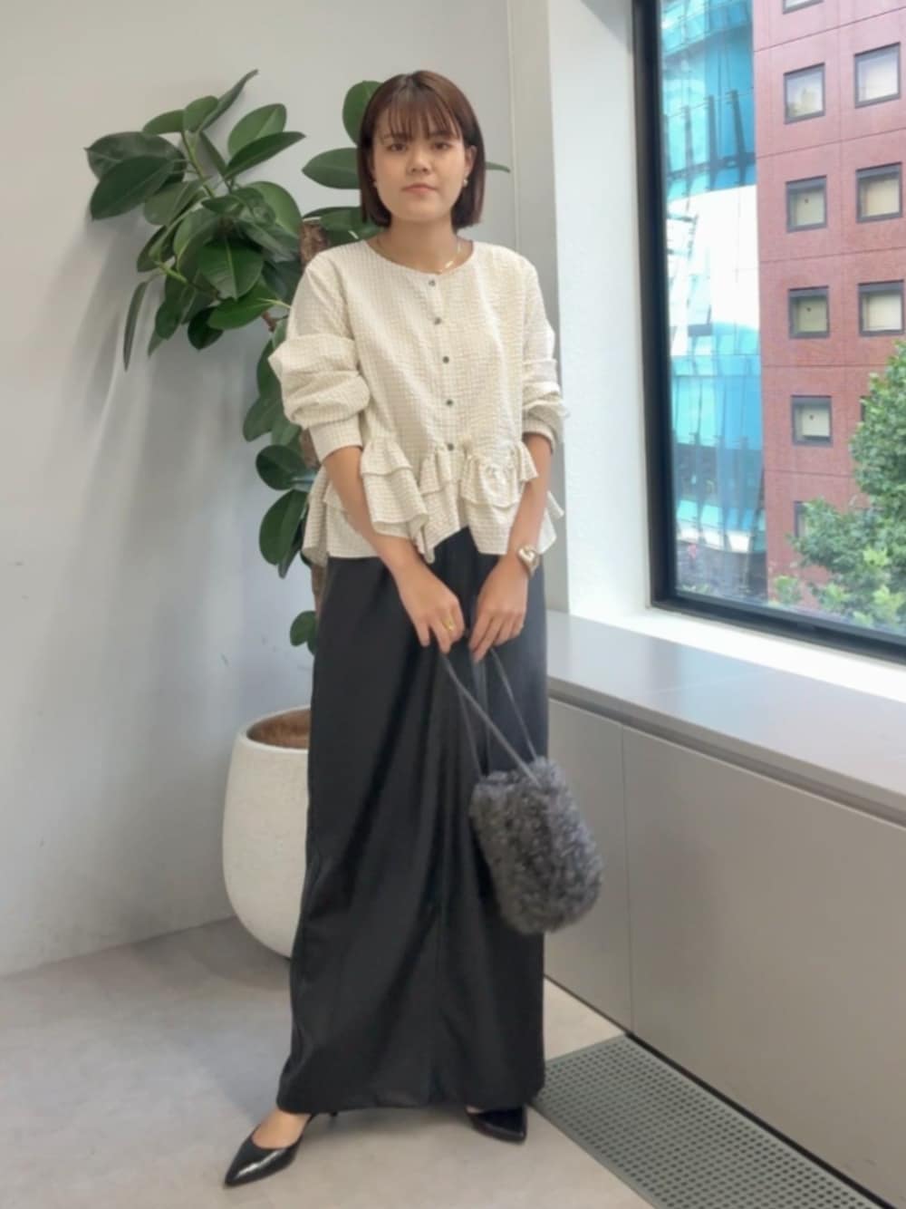 グレー系のハンドバッグ、ブラック系のパンプス、ホワイト系のシャツ/ブラウスを着用したレディースの夏コーディネートの1枚目の写真