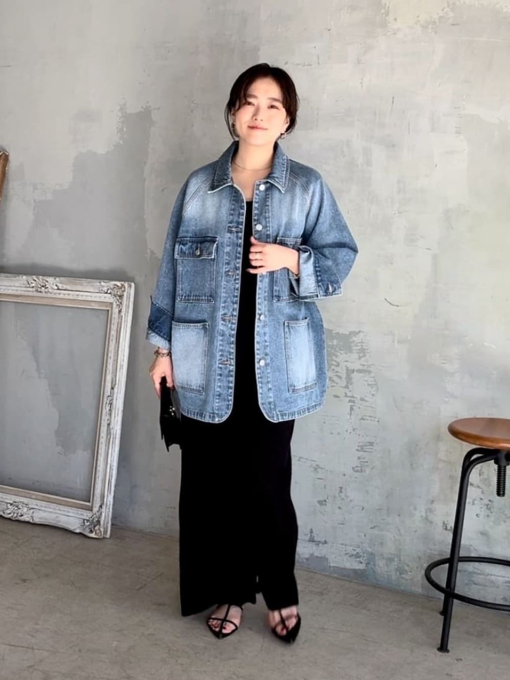 ブルー系のデニムジャケット、ブラック系のワンピース、ブラック系のサンダルを着用したレディースの春コーディネートの1枚目の写真