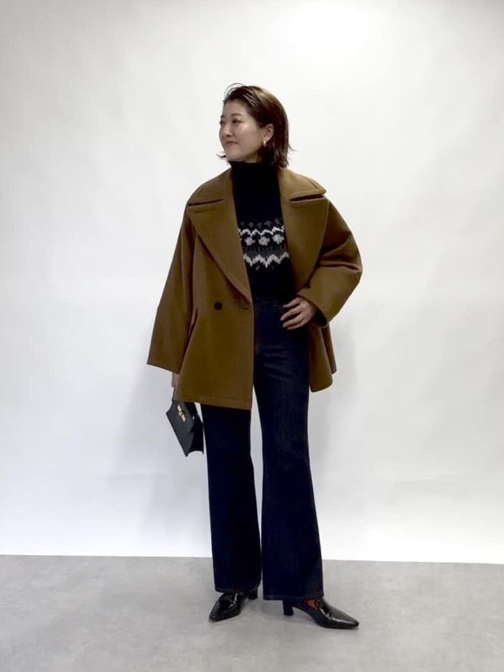 イエロー系のピーコート、ブルー系のデニムパンツ、ブラック系のニット/セーターを着用したレディースの冬コーディネートの1枚目の写真