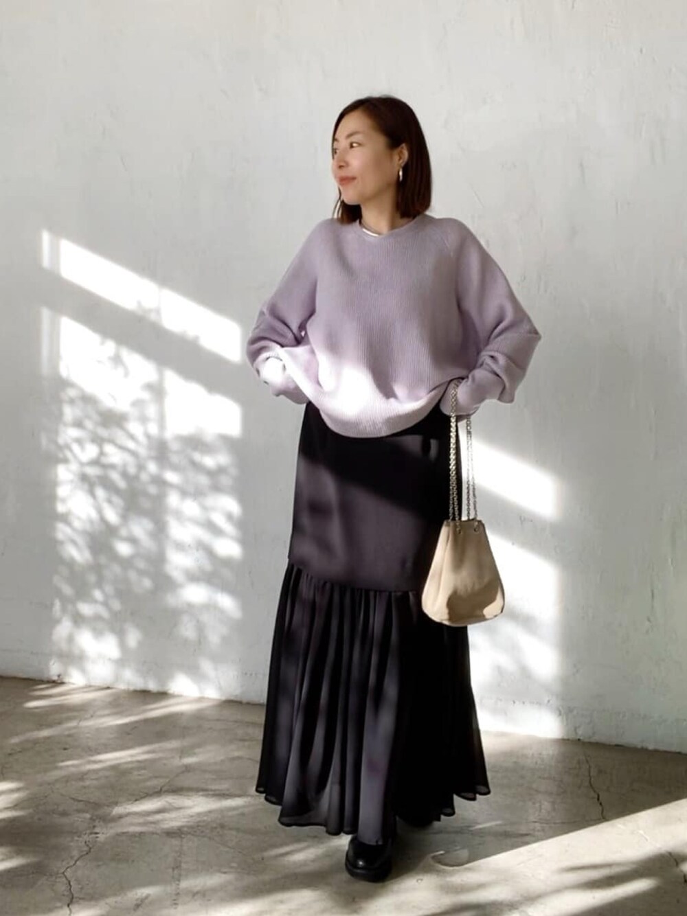 パープル系のニット/セーター、ベージュ系のショルダーバッグ、ブラック系のスカートを着用したレディースの冬コーディネートの1枚目の写真
