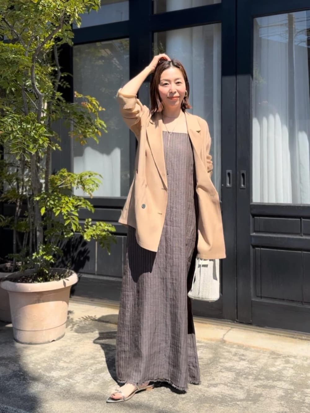 ブラック系のテーラードジャケット、ブラウン系のワンピース、シルバー系のサンダルを着用したレディースの春コーディネートの1枚目の写真