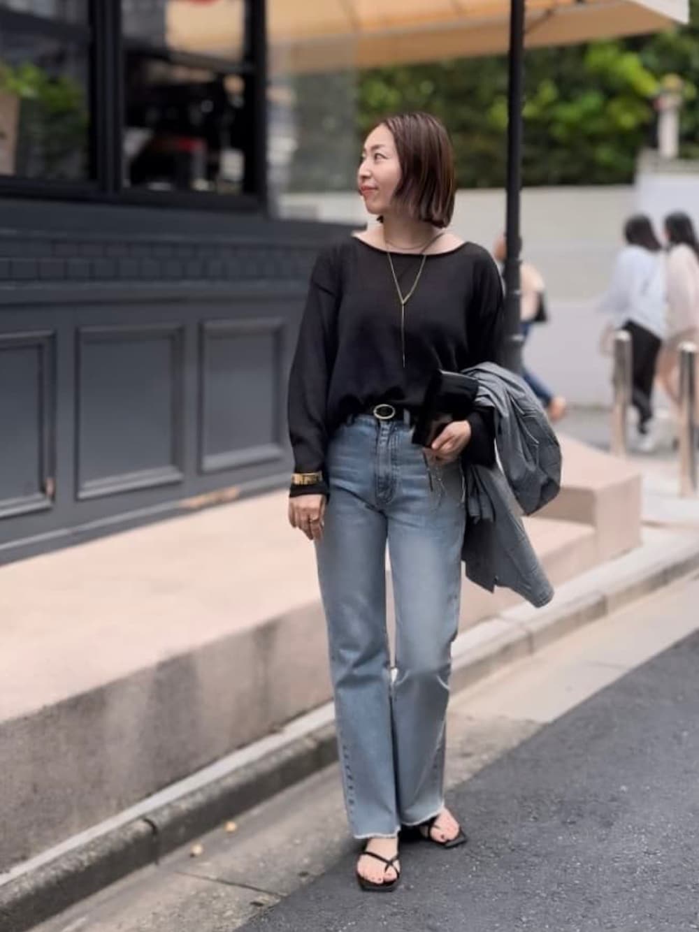 ブラック系のニット/セーター、ブルー系のデニムパンツ、ブラック系のサンダルを着用したレディースの春コーディネートの1枚目の写真
