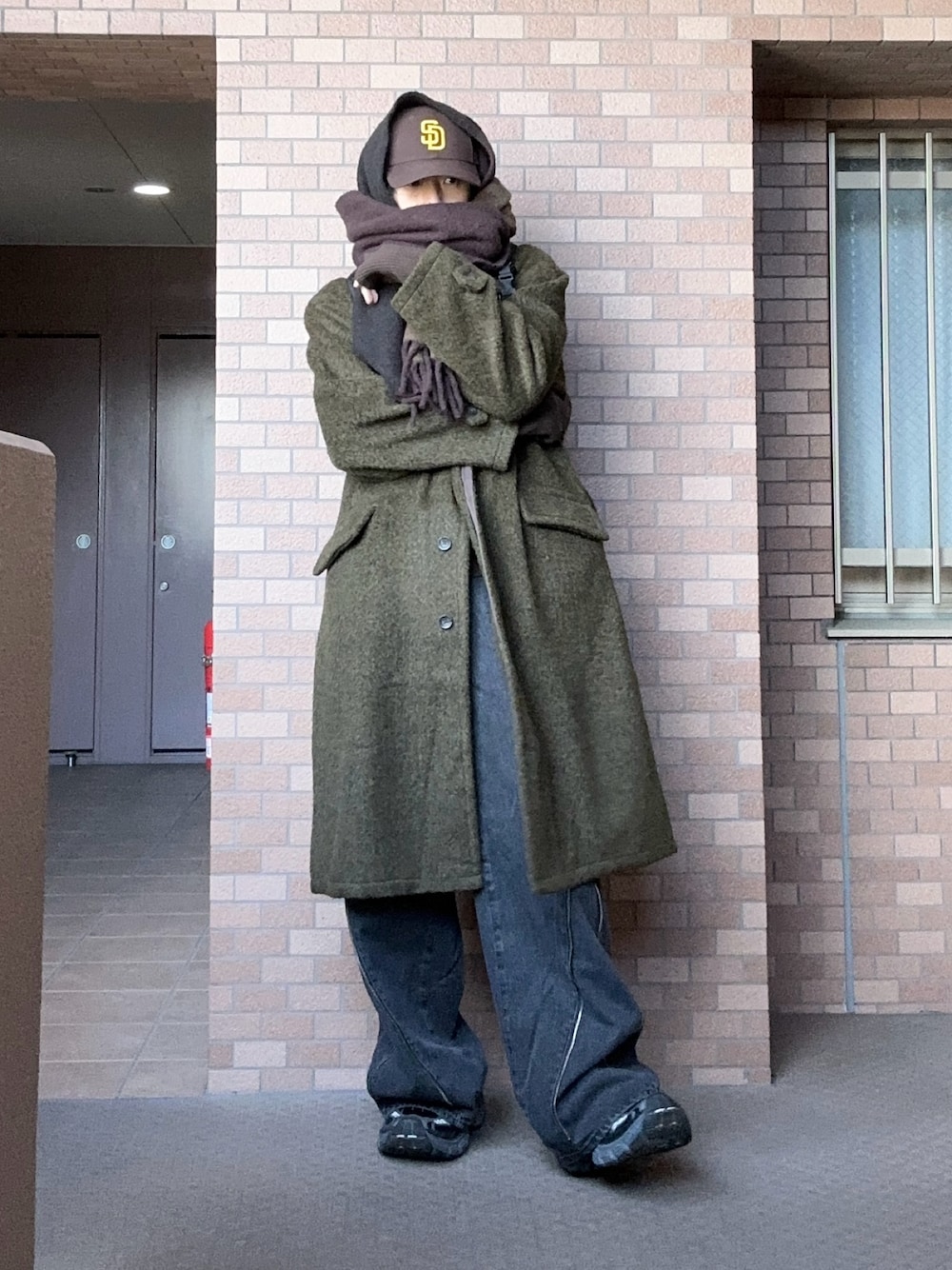 ブラック系のデニムパンツ、ブラウン系のステンカラーコート、ブラック系のスニーカーを着用したメンズの冬コーディネートの1枚目の写真