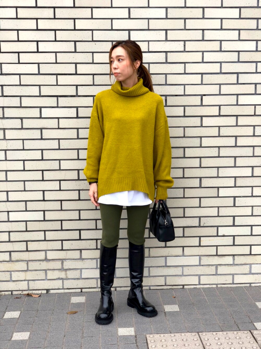 イエロー系のニット/セーター、ブラック系のブーツ、グリーン系のレギンス/スパッツを着用したレディースの秋コーディネートの1枚目の写真