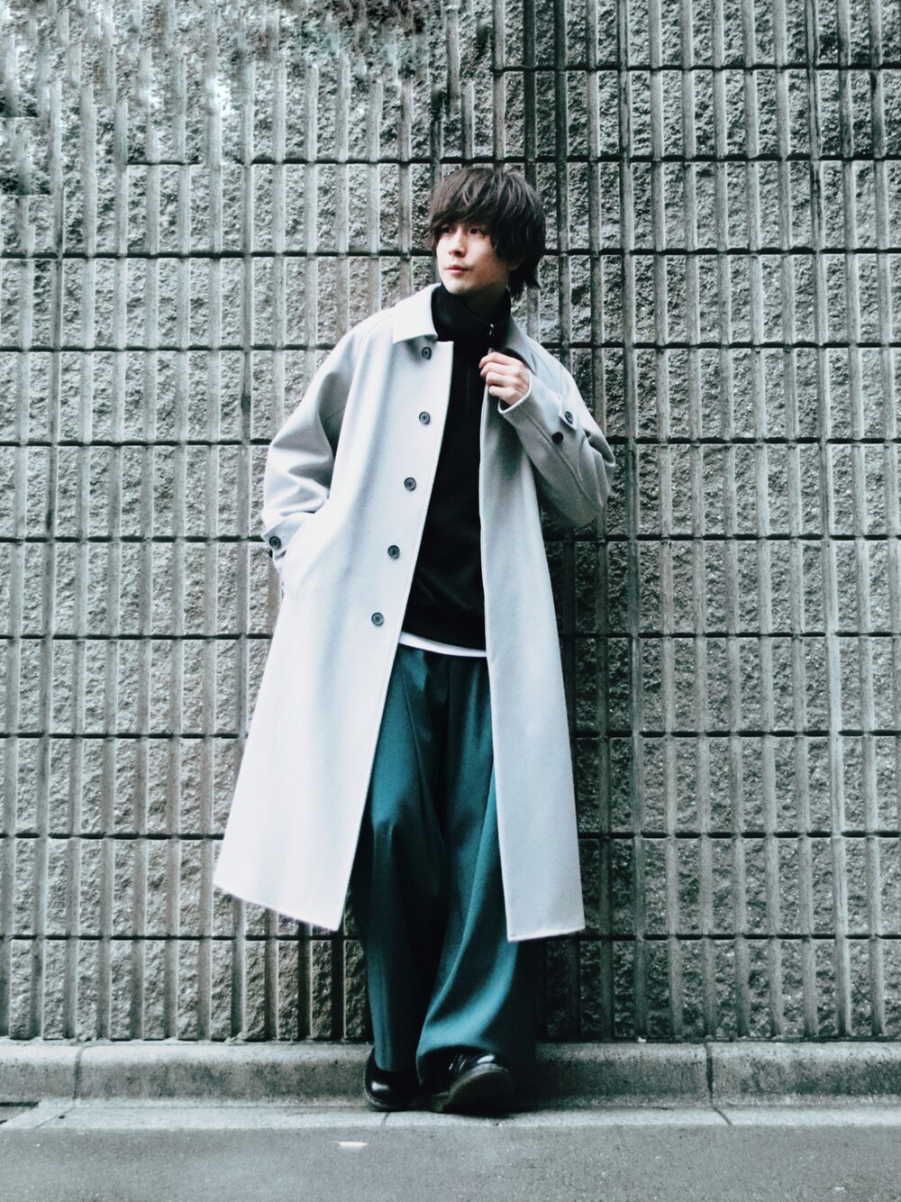 グレー系のステンカラーコート、ブラック系のトップス、グリーン系のスラックスを着用したメンズの冬コーディネートの1枚目の写真