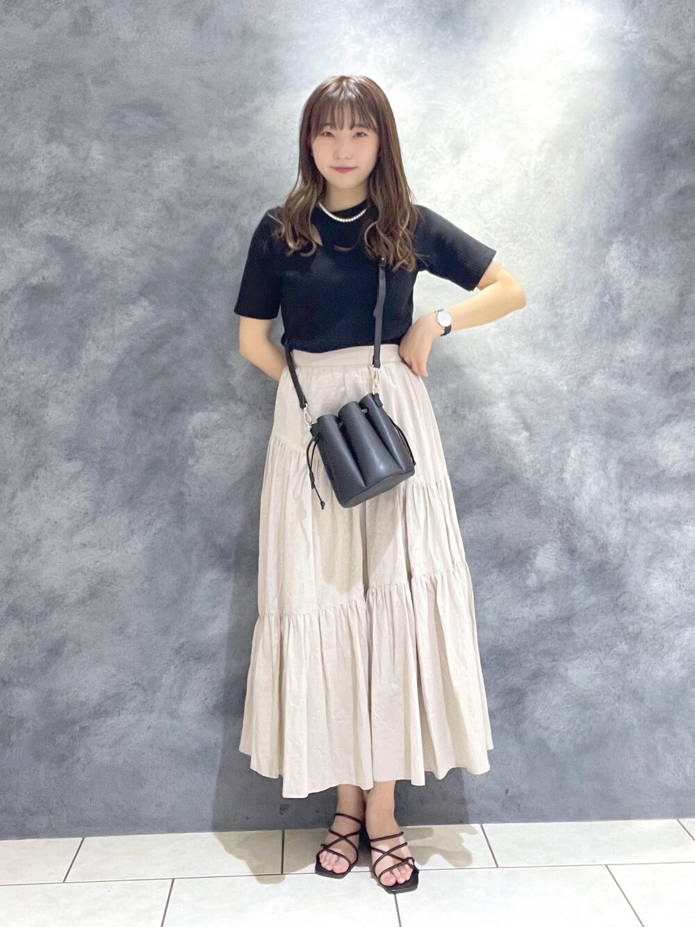 ベージュ系のスカート、ブラック系のサンダル、ブラック系のショルダーバッグを着用したレディースの夏コーディネートの1枚目の写真