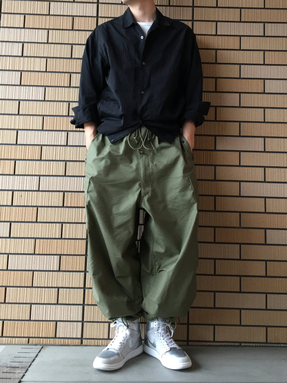 グリーン系のカーゴパンツ、シルバー系のスニーカー、ブラック系のシャツ/ブラウスを着用したメンズの春コーディネートの1枚目の写真