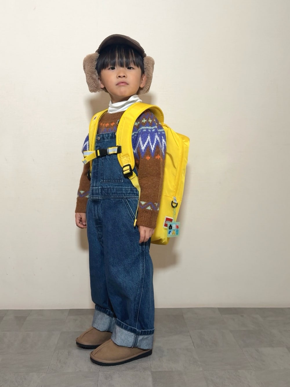 イエロー系のブーツ、イエロー系のバックパック/リュック、ブラウン系のニット/セーターを着用したキッズの冬コーディネートの1枚目の写真