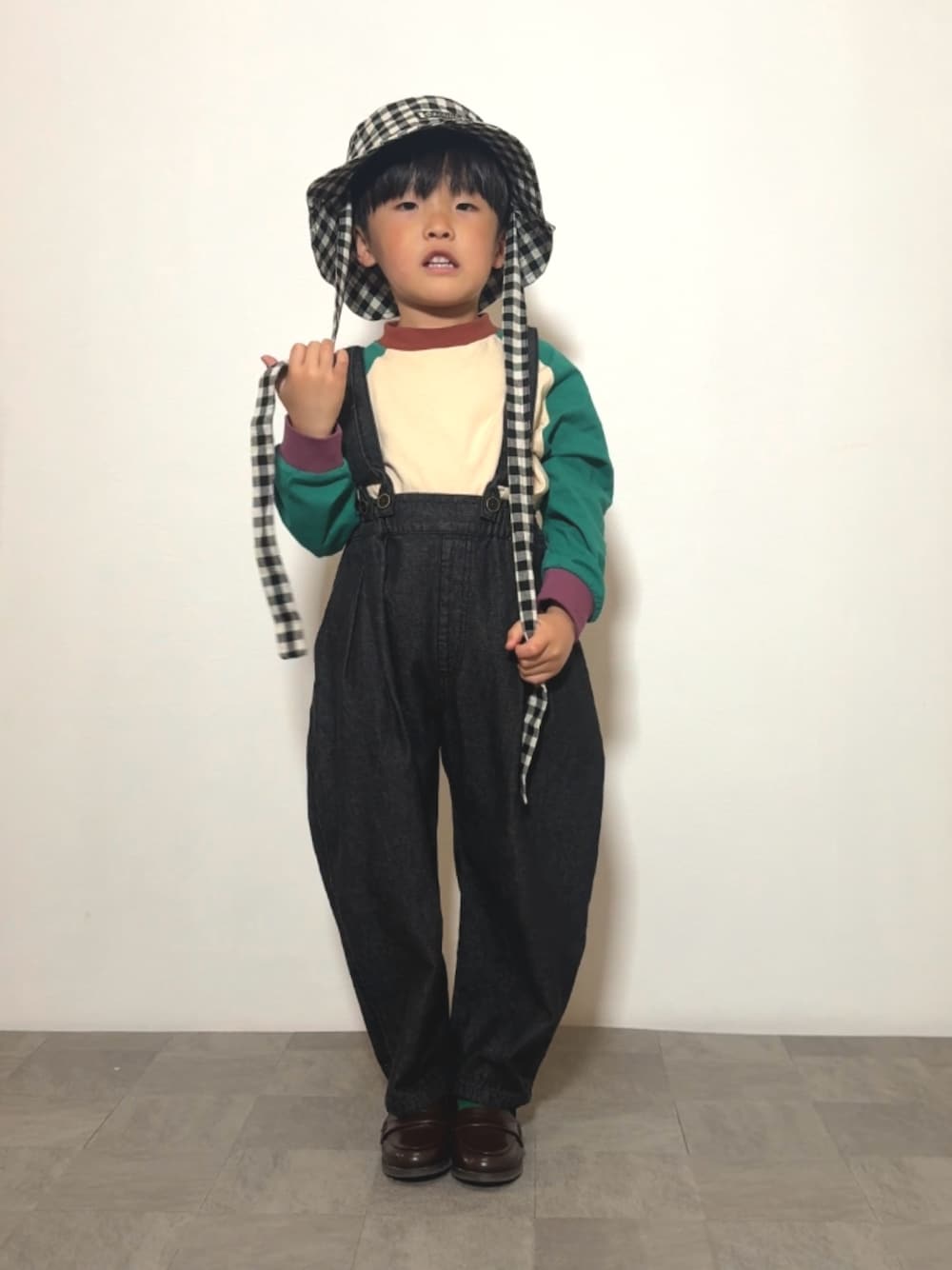 ブラック系のサロペット/オーバーオール、ブラウン系のローファー、グリーン系のTシャツ/カットソーを着用したキッズの春コーディネートの1枚目の写真