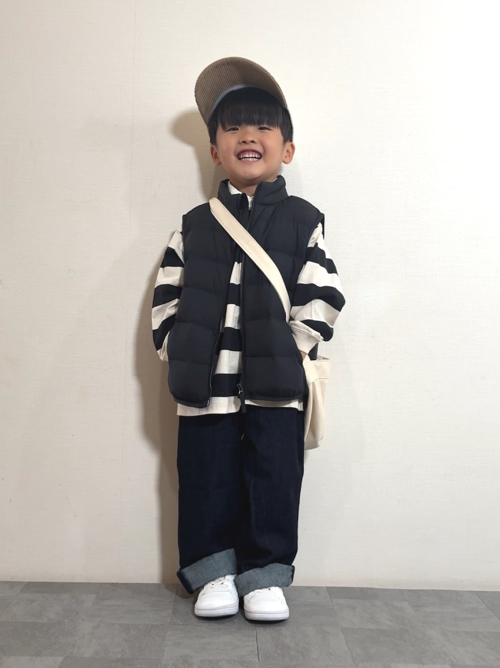 ホワイト系のスニーカー、ブラック系のベスト、ホワイト系のポロシャツを着用したキッズの秋コーディネートの1枚目の写真