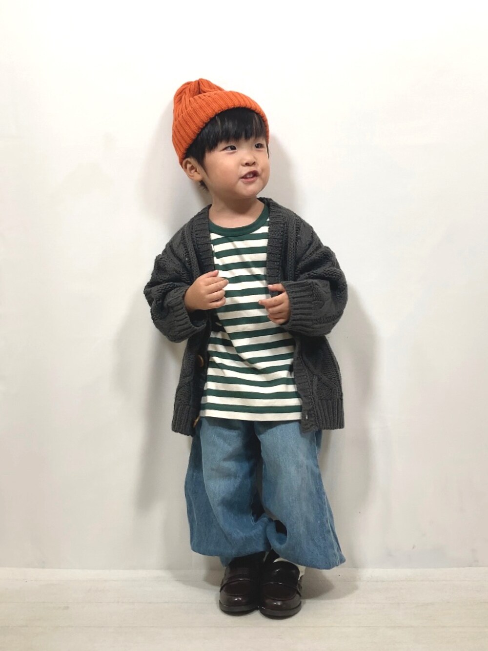 グレー系のカーディガン/ボレロ、グリーン系のTシャツ/カットソー、ブルー系のデニムパンツを着用したキッズの秋コーディネートの1枚目の写真