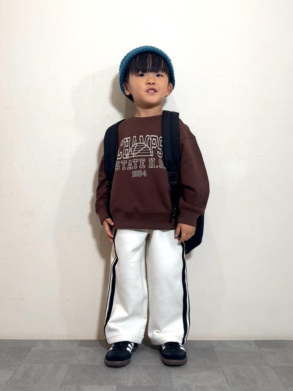 ブラック系のスニーカー、ブラック系のバックパック/リュック、ブラウン系のスウェットを着用したキッズの秋コーディネートの1枚目の写真