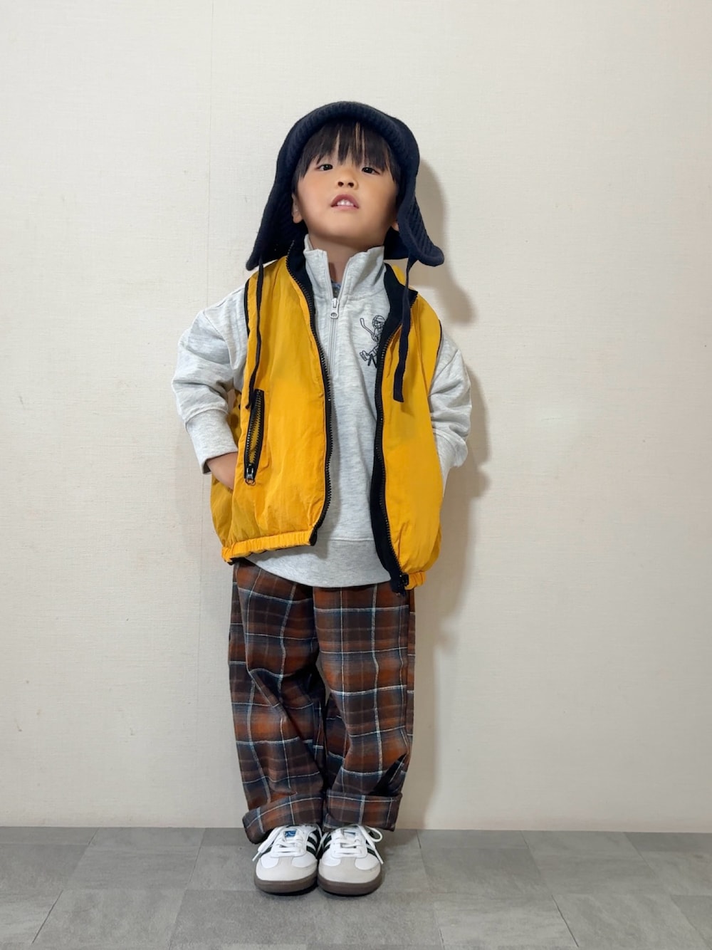 イエロー系のベスト、ホワイト系のスニーカー、グレー系のスウェットを着用したキッズの秋コーディネートの1枚目の写真