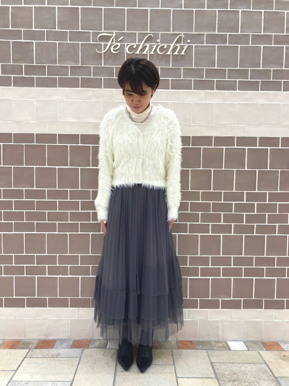 ホワイト系のニット/セーター、グレー系のスカート、ホワイト系のTシャツ/カットソーを着用したレディースの秋コーディネートの1枚目の写真