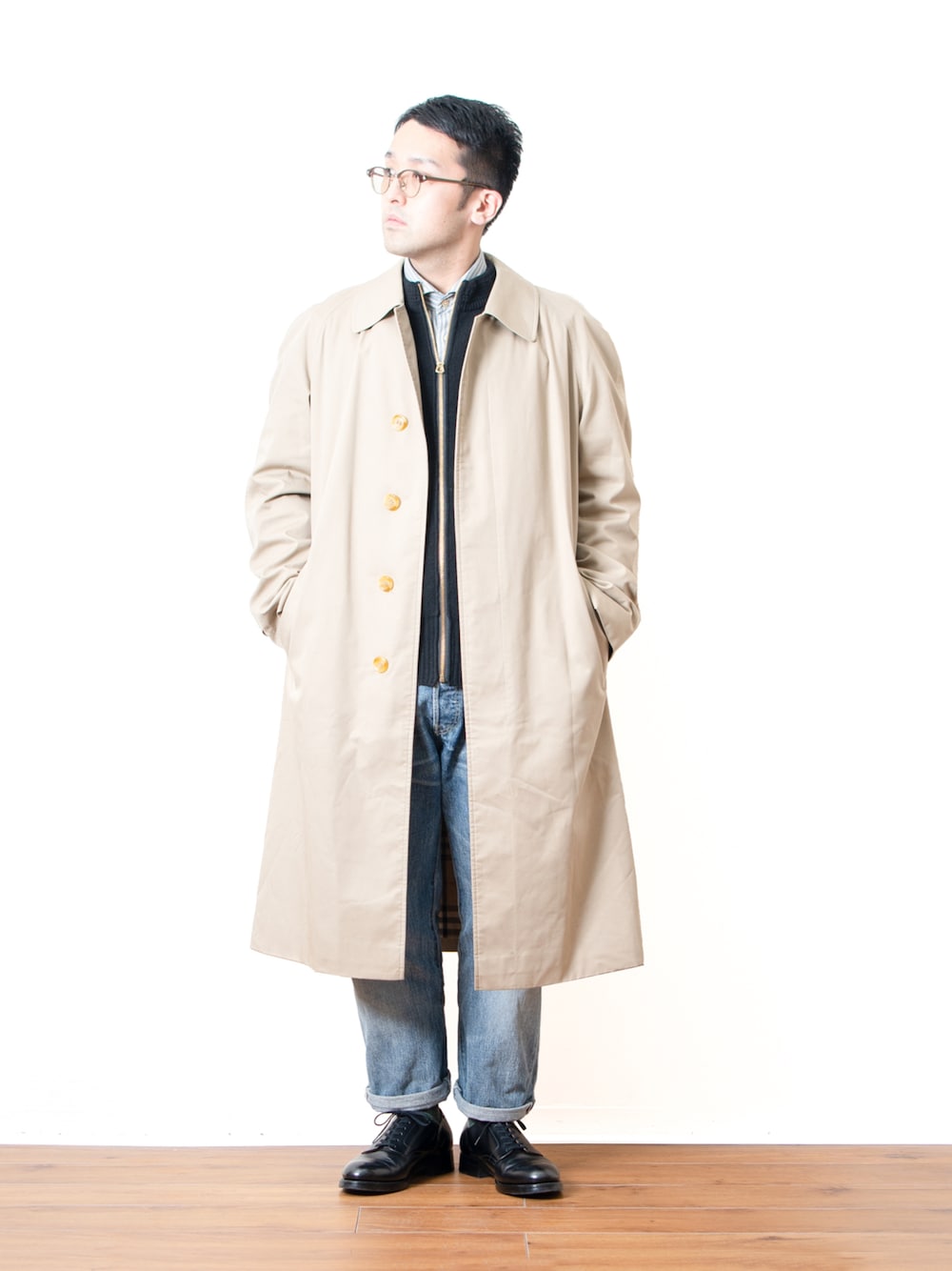 ブルー系のデニムパンツ、ブラック系のニット/セーター、ベージュ系のステンカラーコートを着用したメンズの春コーディネートの1枚目の写真