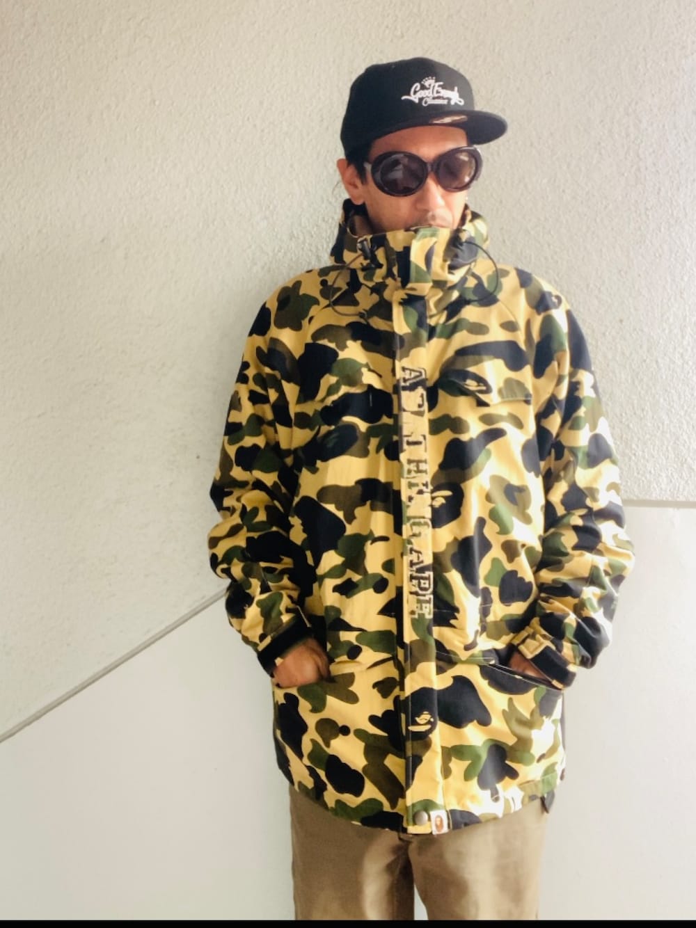 イエロー系のマウンテンパーカー、グリーン系のカーゴパンツ、ブラック系のブーツを着用したメンズの秋コーディネートの1枚目の写真