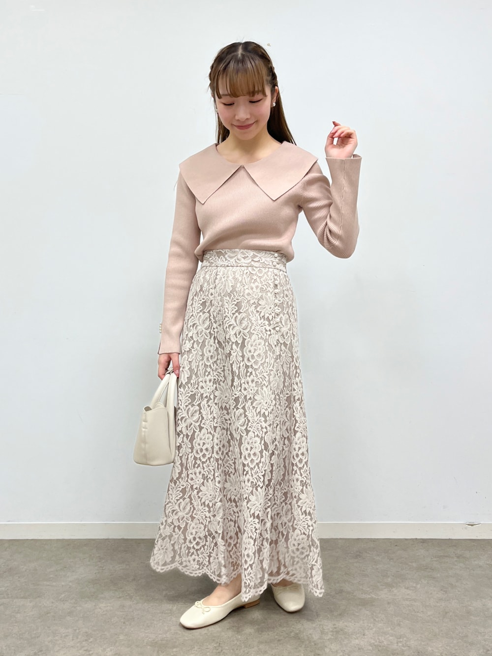ピンク系のニット/セーター、ベージュ系のスカート、ホワイト系のショルダーバッグを着用したレディースの冬コーディネートの1枚目の写真
