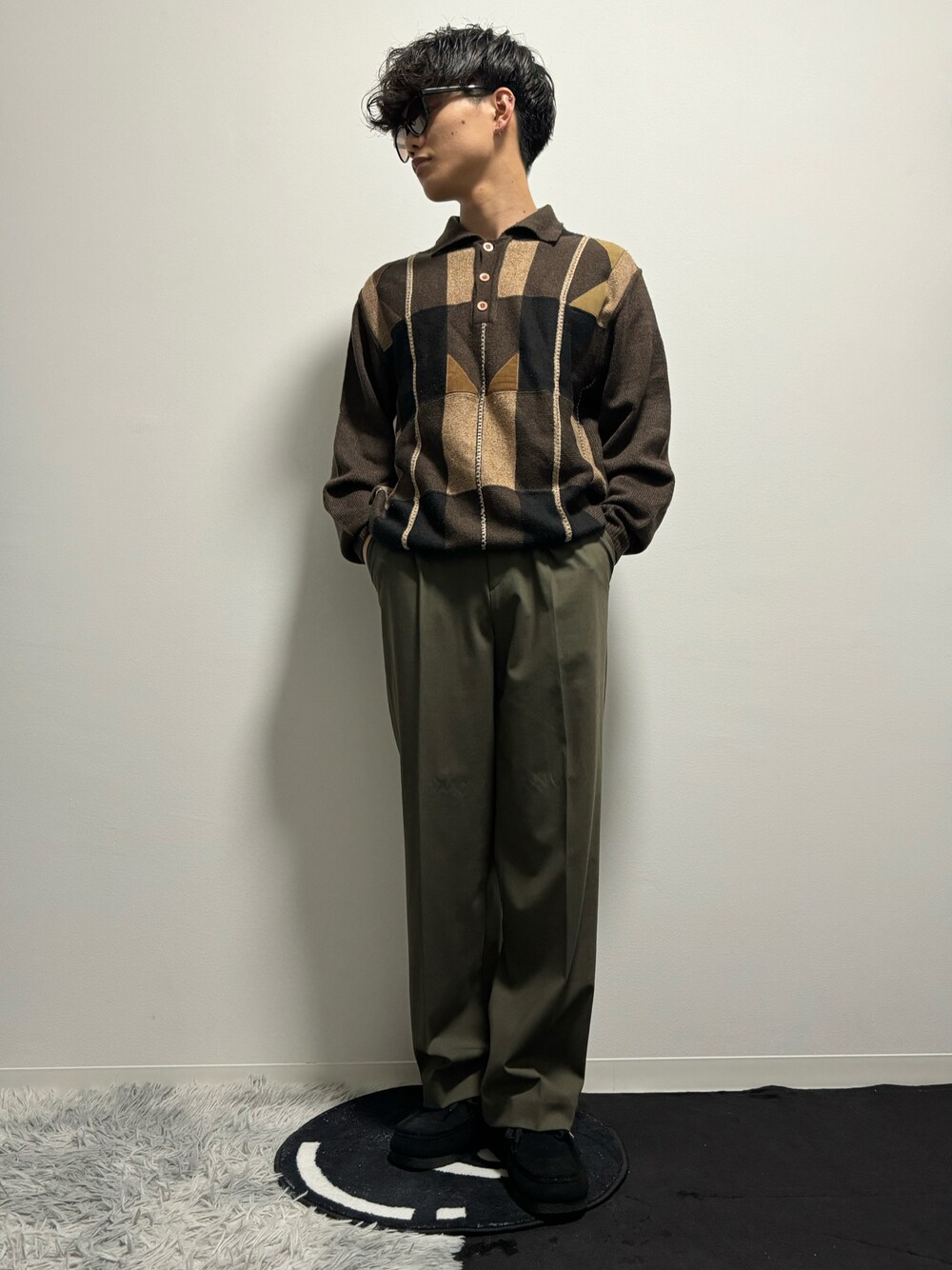 グリーン系のスラックス、ブラック系のモカシン/デッキシューズ、ブラウン系のポロシャツを着用したメンズの春コーディネートの1枚目の写真