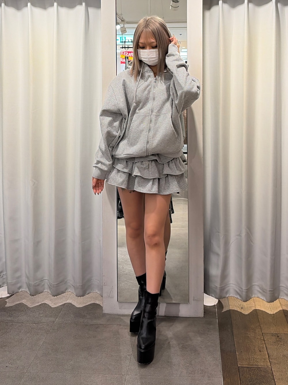 グレー系のパーカー、ブラック系のスカート、ブラック系のブーツを着用したレディースの冬コーディネートの1枚目の写真