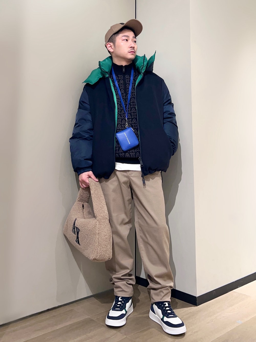 グリーン系のスニーカー、ベージュ系のチノパンツ、ベージュ系のハンドバッグを着用したメンズの冬コーディネートの1枚目の写真